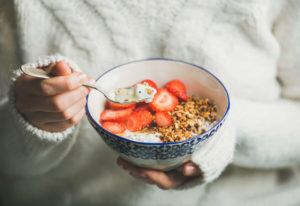 woman holding a bowl of granola, yogurt, and strawberries