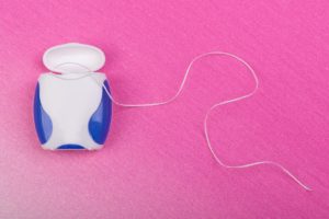 Container of tooth floss on a pink background