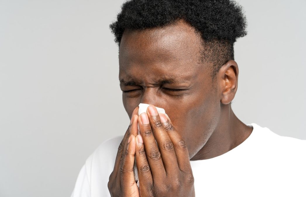 man sneezing into a tissue due to seasonal allergies that are causing him some tooth pain