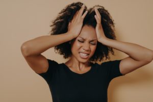 black woman with hands on her head and teeth clinched showing she's stressed